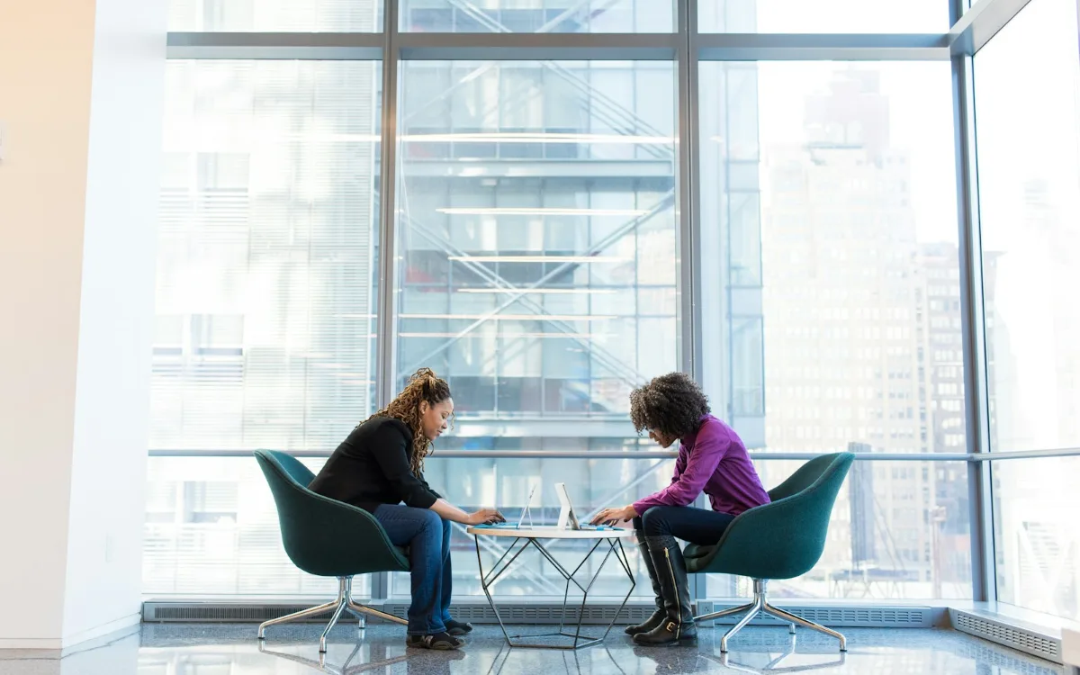 Deux professionnels en discussion de part et d'autre d'une table basse, devant une baie vitrée.